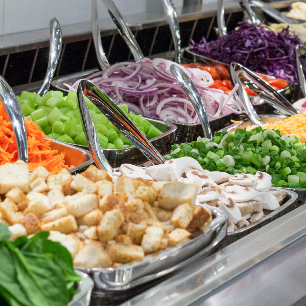 An array of salad options, such as onions, croutons, & carrots, from the full service salad bar at Freson Bros. Fresh Market Kitchens